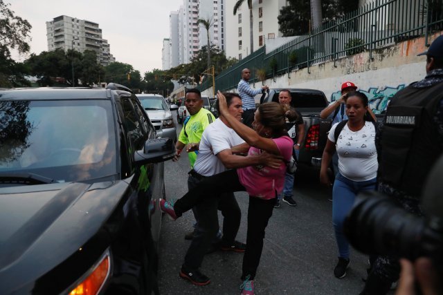 A supporter of Venezuelan President Nicolas Maduro attempts to kick a car which is part of a convoy transporting opposition leader Juan Guaido in Caracas