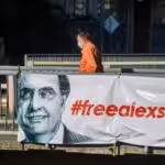 Featured image: Posters in the streets of Caracas demanding the release of Alex Saab. Photo courtesy of Getty Images.
