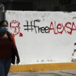 A pedestrian passes in front of “Free Alex Saab” graffiti “ in Caracas, on Feb. 4. Photographer: Carlos Becerra/Bloomberg.
