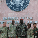 Coup leader Colonel Doumbouya smiling for a photo in front of the US Embassy and escorted by AFRICOM officers. Photo courtesy of Twiter / @kambale.