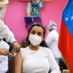 Venezuelan woman being inoculated with an anti COVID-19 vaccine, next to a Venezuelan flag. File photo.