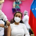 Venezuelan woman being inoculated with an anti COVID-19 vaccine, next to a Venezuelan flag. File photo.
