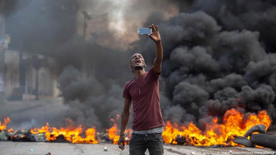 Protester in Haiti taking a selfie with burning fires in the background. File photo by Odelyn Joseph/AP/DPA.