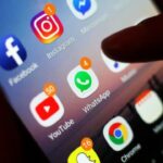 Person holding a smartphone with social media platform apps. Referential photo.