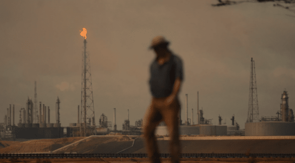 Featured image: A man stands in front of an oil plant. Photo: AP Photo / Natacha Pisarenko. 
