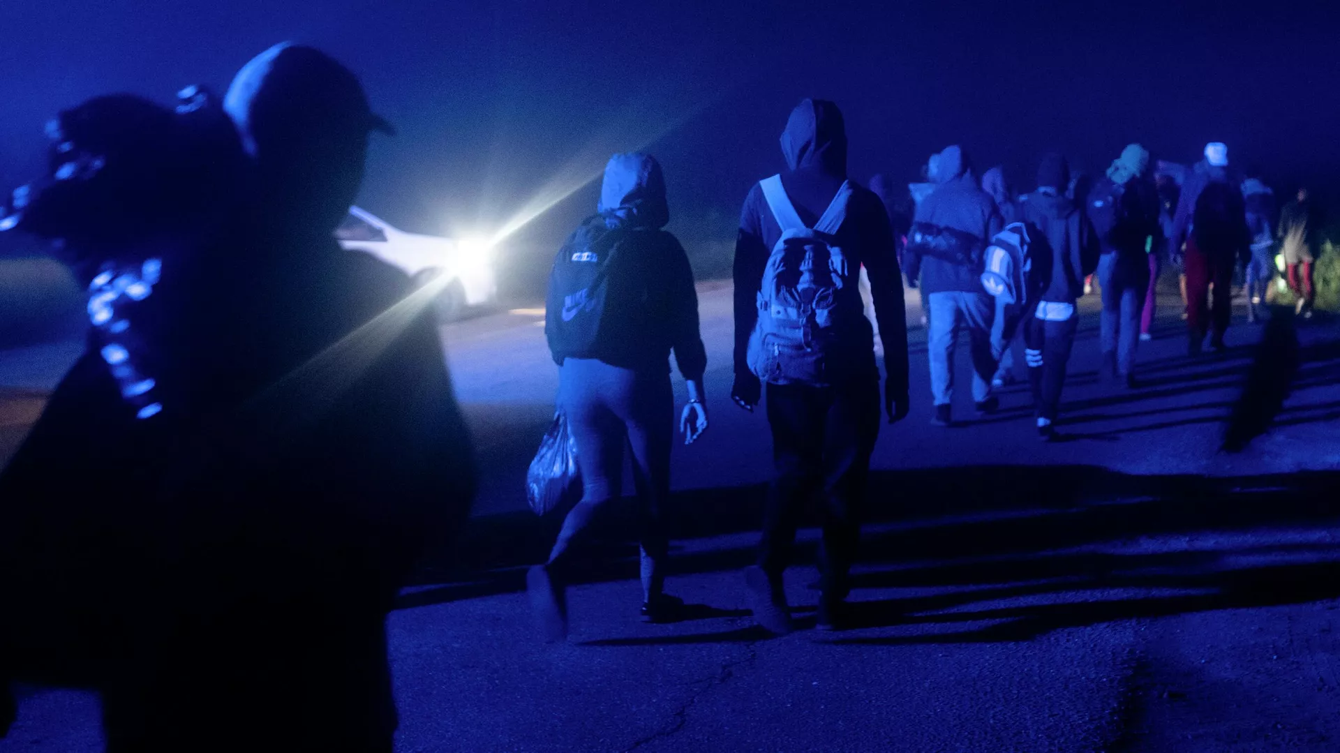 Migrants walking in line during the night while a car provide them with some light. Photo: AP/Felix Marquez.