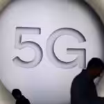 Silhouette of two persons looking at their cellphone with a big 5G logo as background. File photo.