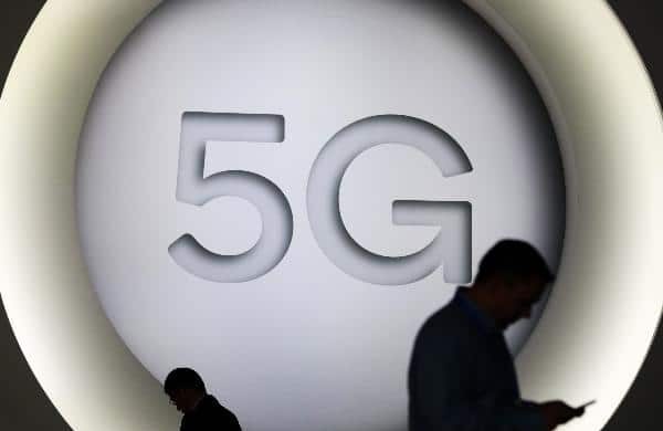 Silhouette of two persons looking at their cellphone with a big 5G logo as background. File photo.