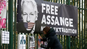 Activist adding placards near a big banner with a photo of Julian Assange with his mouth strapped with the US flag. The banner reads "Free Assange, No Extradition." Photo: Reuters/Henry Nicholls.