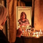 A woman lights a candle in front of a poster of veteran Palestinian journalist Shireen Abu Akleh, who was shot dead while covering an Israeli army raid in Jenin, at the the Church of the Nativity in the West Bank city of Bethlehem, on May 11, 2022. Photo: AFP.