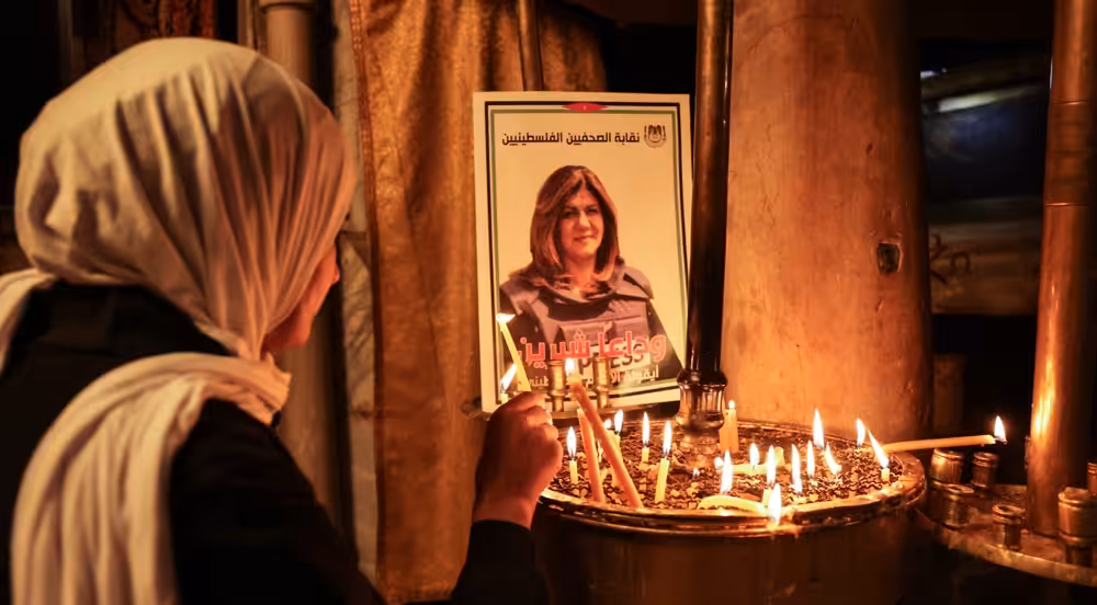 A woman lights a candle in front of a poster of veteran Palestinian journalist Shireen Abu Akleh, who was shot dead while covering an Israeli army raid in Jenin, at the the Church of the Nativity in the West Bank city of Bethlehem, on May 11, 2022. Photo: AFP.