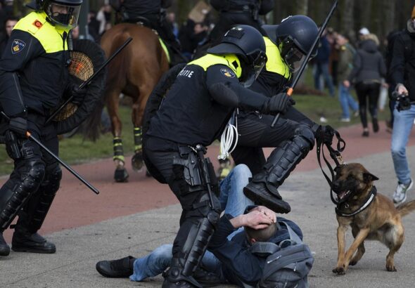 Dutch riot police kick a man during a demonstration to protest government policies including COVID-19 curfew, lockdown, and related restrictions in The Hague. Photo: Peter Dejong/AP.
