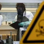 Two workers wearing bio-security gear and taking notes behind a warning sign. File photo.