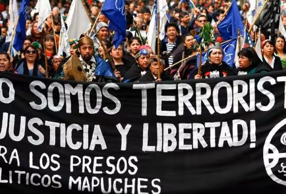 Indigenous Mapuche activist in a street protest holding a banner that reads: "We are not terrorists! Justice and freedom for Mapuche political prisioners." Photo: IWGIA.