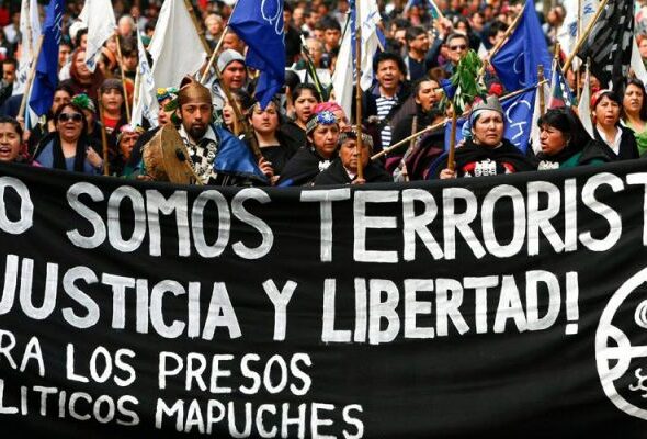 Indigenous Mapuche activist in a street protest holding a banner that reads: "We are not terrorists! Justice and freedom for Mapuche political prisioners." Photo: IWGIA.