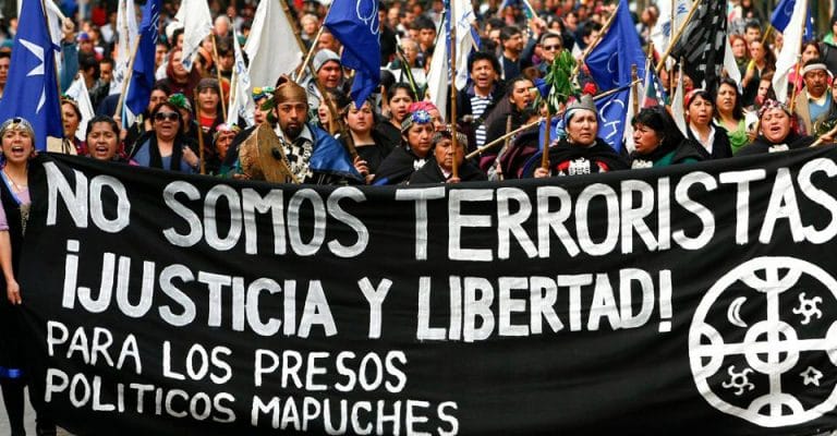 Indigenous Mapuche activist in a street protest holding a banner that reads: "We are not terrorists! Justice and freedom for Mapuche political prisioners." Photo: IWGIA.