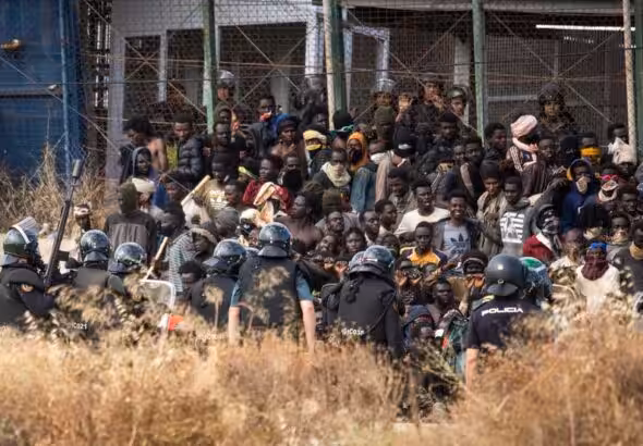 Police in riot gear contain migrants attempting to breach the border fence of the Spanish enclave of Melilla. Photo: Javier Bernardo/AP.