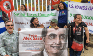 US and Venezuelan activist participating in the Worker’s Summit of the AMericas in Tijuana during a stand in front of the US/Mexico border wall and hilding a “FreeAlexSaab banner. Photo: Roger D. Harris