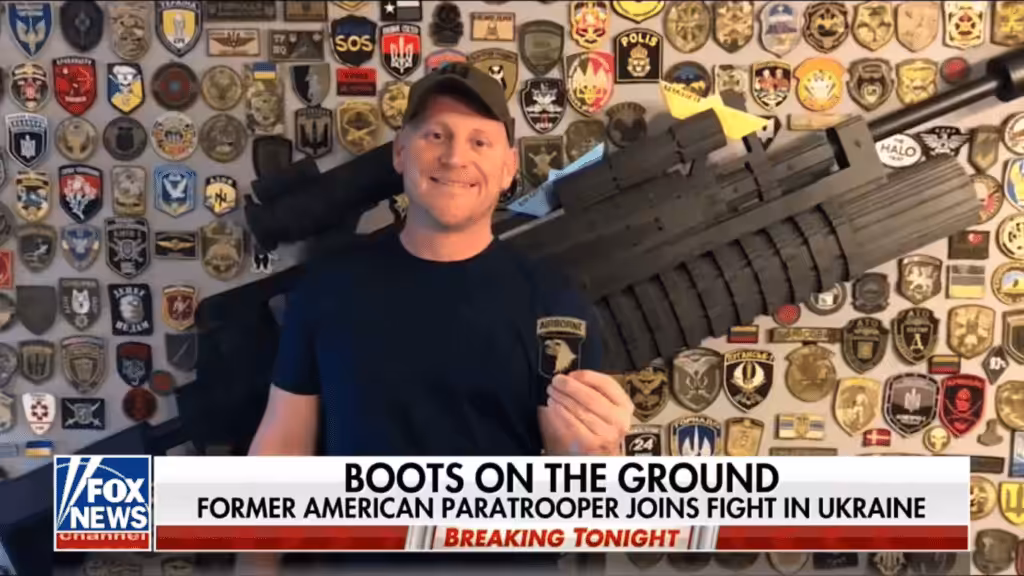 American neo-Nazi Paul Gray on Fox News in front of a wall featuring emblems of fascist militias like the Azov Battallion. Photo: Author