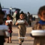Syrian children in a refugee camp holding boxes of food delivered by humanitarian organizations. Syria is suffering an extreme food shortage as US-NATO forces continue to steal wheat from occupied north-eastern Syria. Photo: Syria News.