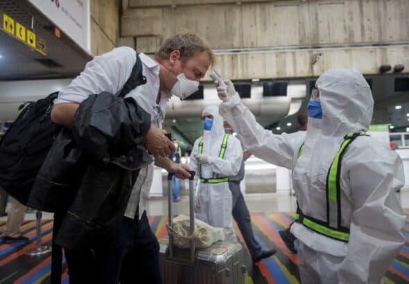 A health worker takes the temperature of European citizens who will take a flight to Madrid, at the Simon Bolivar International Airport in Maiquetia, in La Guaira, Caracas, Venezuela, 26 March 2020. Photo: EPA/Rayner Pena R