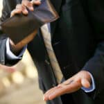 Man showing some coins after squeezing his wallet. Photo: New Eastern Outlook.