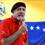 Carlos Lanz giving a speech wearing a red shirt and black beret, with a Venezuelan flag in the background. File photo.