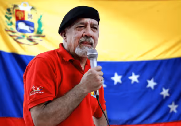 Carlos Lanz giving a speech wearing a red shirt and black beret, with a Venezuelan flag in the background. File photo.