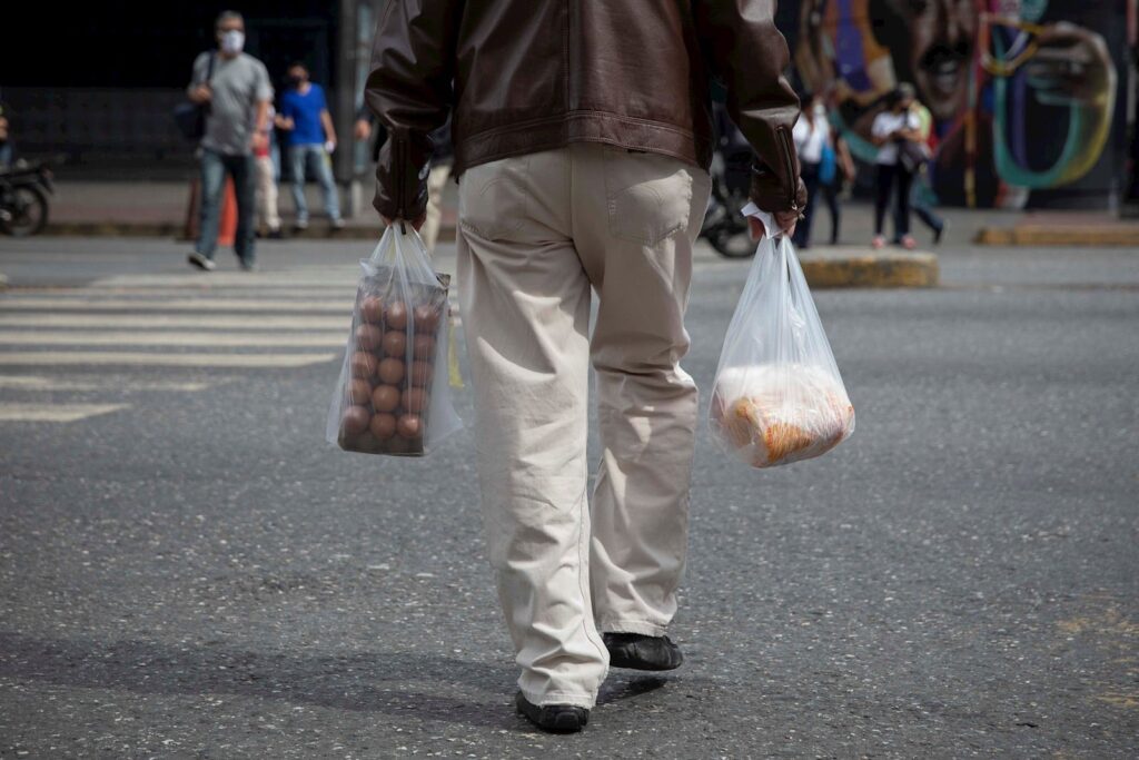 Person crossing the street in Caracas while holding grocery bags. Photo: EFE.