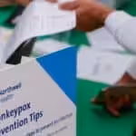 Person showing some papers to an attendant near a sign that reads “Monkeypox Prevention Tips.” Photo: Beijing News/Twitter.