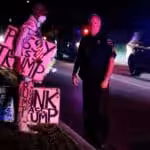 A man carrying Trump posters and wearing a hat with US flag colors stands in front of a policeman. Photo: Eva Marie Uzcategui/Getty Images.