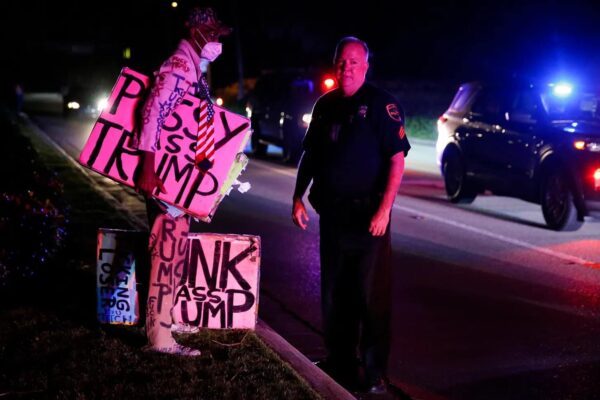A man carrying Trump posters and wearing a hat with US flag colors stands in front of a policeman. Photo: Eva Marie Uzcategui/Getty Images.