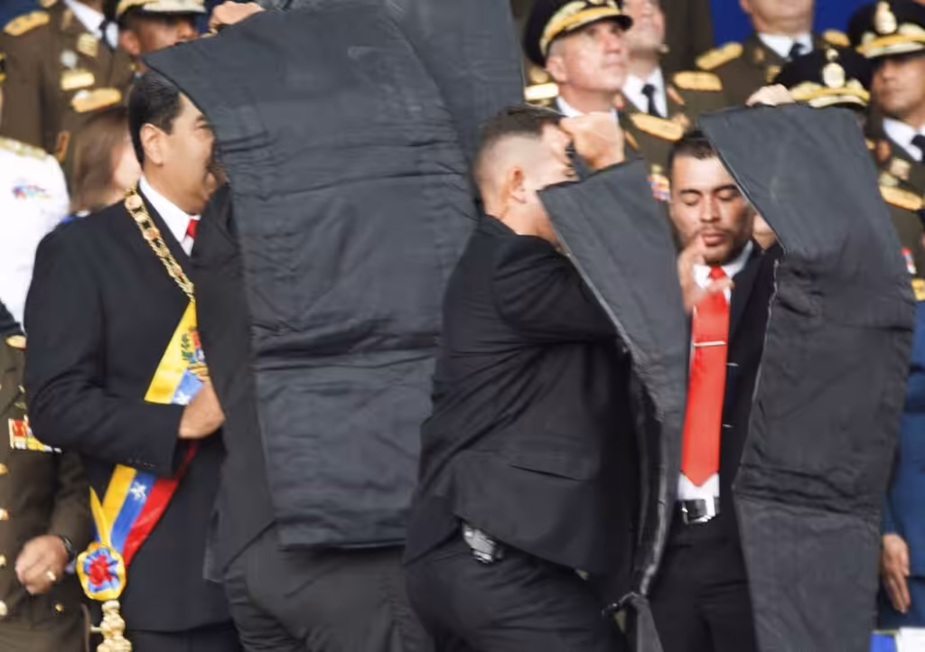 In this photo released by China's Xinhua News Agency, security personnel surround Venezuela's President Nicolás Maduro, left, after drones armed with explosives detonated as he was making a speech in Caracas, Venezuela, Aug. 4, 2018.