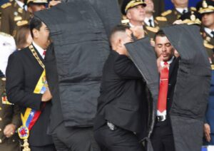 In this photo released by China's Xinhua News Agency, security personnel surround Venezuela's President Nicolas Maduro, at left, after drones armed with explosives detonated as he was giving a speech in Caracas, Venezuela, Aug. 4, 2018.