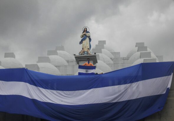 Giant Nicaraguan flag waving below the figure of a saint and a person holding a small Nicaraguan flag. File photo.