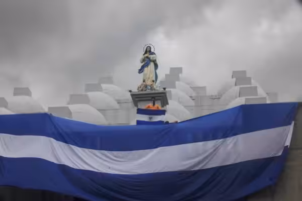 Giant Nicaraguan flag waving below the figure of a saint and a person holding a small Nicaraguan flag. File photo.