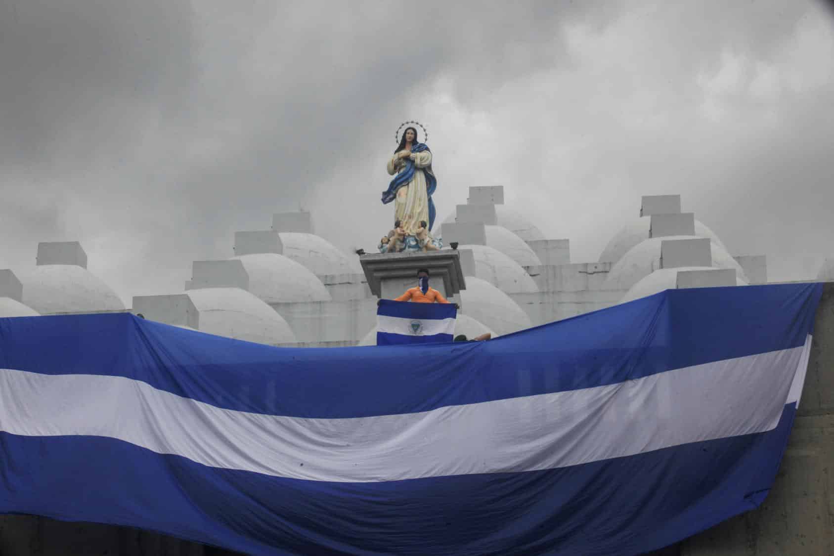 Giant Nicaraguan flag waving below the figure of a saint and a person holding a small Nicaraguan flag. File photo.