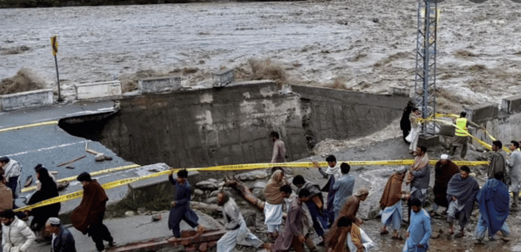 People gather in front of a road damaged by flood waters following heavy monsoon rains in Madian area in Pakistan’s northern Swat Valley on August 27, 2022. Photo: AFP.