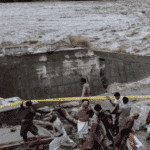 People gather in front of a road damaged by flood waters following heavy monsoon rains in Madian area in Pakistan’s northern Swat Valley on August 27, 2022. Photo: AFP.