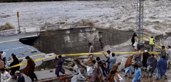 People gather in front of a road damaged by flood waters following heavy monsoon rains in Madian area in Pakistan’s northern Swat Valley on August 27, 2022. Photo: AFP.