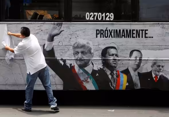 A man tears an advertising campaign featuring leftist front-runner Andres Manuel Lopez Obrador (L) of the National Regeneration Movement (MORENA) alongside Latin American leaders Hugo Chavez and Lula in Mexico City, Mexico April 25, 2018. Photo: REUTERS/Ginnette Riquelme.