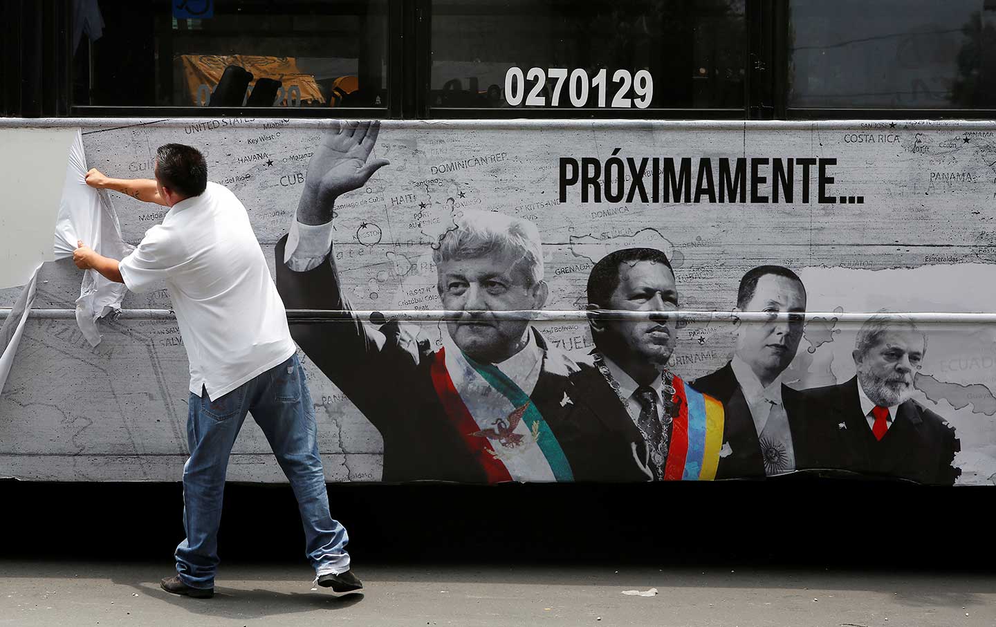 A man tears an advertising campaign featuring leftist front-runner Andres Manuel Lopez Obrador (L) of the National Regeneration Movement (MORENA) alongside Latin American leaders Hugo Chavez and Lula in Mexico City, Mexico April 25, 2018. Photo: REUTERS/Ginnette Riquelme.