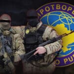 Photographic composition that shows two uniformed Ukrainians with their eyes crossed out in front and the symbol of the Mirotvorets organization in the background. File photo.