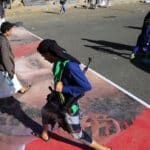 People walking over a street paint with the face of French President Emmanuel Macron. Photo: AFP/Mohammed HUWAIS.
