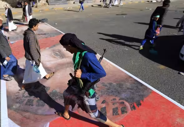 People walking over a street paint with the face of French President Emmanuel Macron. Photo: AFP/Mohammed HUWAIS.