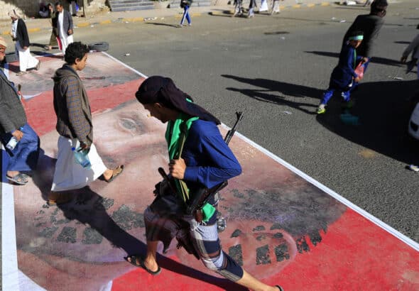 People walking over a street paint with the face of French President Emmanuel Macron. Photo: AFP/Mohammed HUWAIS.