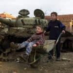 Two Kosovar boys play with a wheelbarrow January 12, 2001 in Klina, Kosovo at one of 112 sites where NATO used armor-piercing shells tipped with depleted uranium during the 1999 bombing of Yugoslavia. Photo: Getty Images/Darko Bandic/Newsmakers.