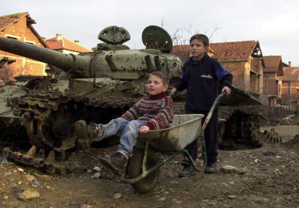 Two Kosovar boys play with a wheelbarrow January 12, 2001 in Klina, Kosovo at one of 112 sites where NATO used armor-piercing shells tipped with depleted uranium during the 1999 bombing of Yugoslavia. Photo: Getty Images/Darko Bandic/Newsmakers.