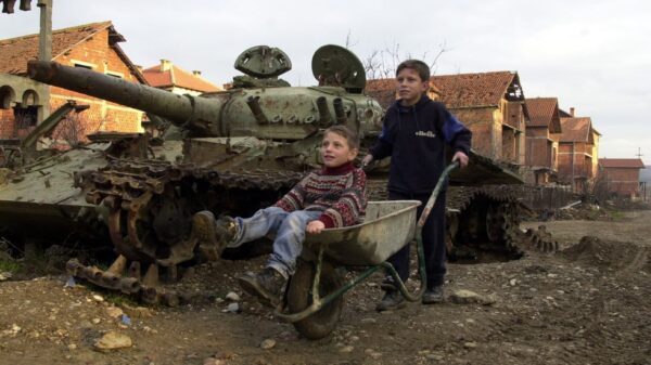 Two Kosovar boys play with a wheelbarrow January 12, 2001 in Klina, Kosovo at one of 112 sites where NATO used armor-piercing shells tipped with depleted uranium during the 1999 bombing of Yugoslavia. Photo: Getty Images/Darko Bandic/Newsmakers.