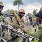 Two heavily armed soldiers in the back of a truck talking with a third one. File photo.